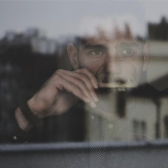 Person partially reflected in a window, suggesting the relationship between constructed identity and deeper self-awareness