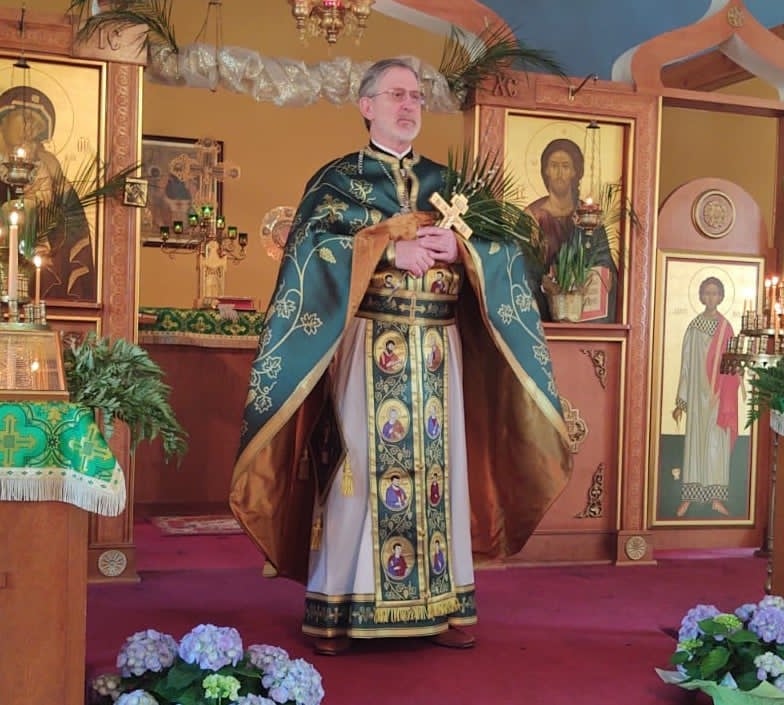 Father Jonathan Ivanoff standing in Orthodox vestments holding a cross during worship, illustrating faith as a lived spiritual practice.