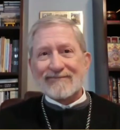Portrait of Father Jonathan Ivanoff, Orthodox priest, educator, and spiritual teacher, seated before a bookshelf and icons.