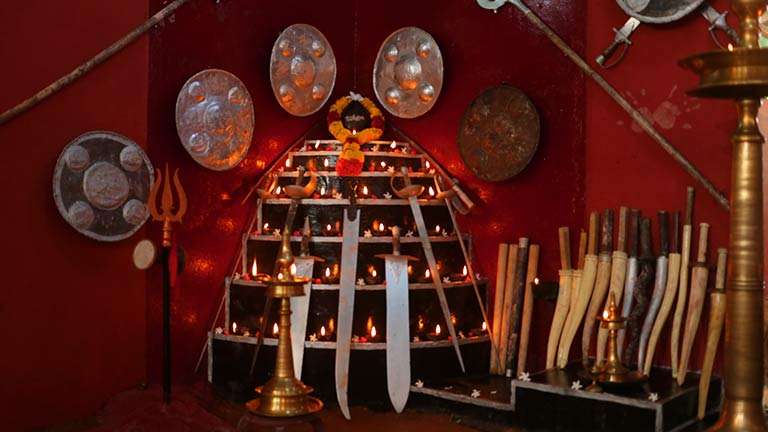 Traditional Kalari ritual altar displaying weapons, lamps, and symbols of lineage within the warrior path of India.