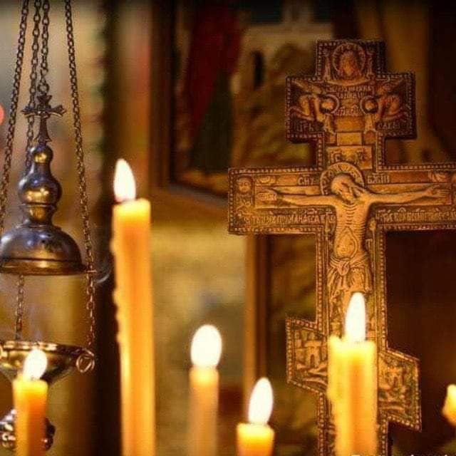Orthodox cross surrounded by burning prayer candles inside a church, symbolizing forgiveness, prayer, spiritual renewal, and transformation.
