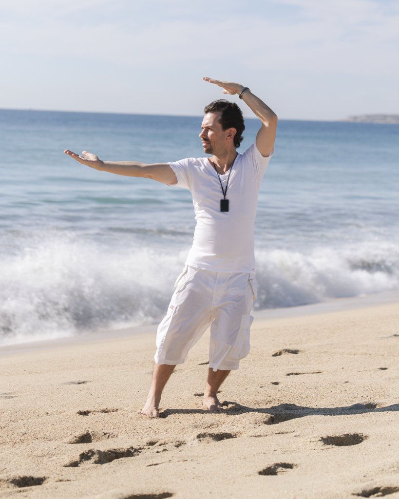 Fabrice Piché practicing qigong beside the ocean, demonstrating movement, attention, and embodied awareness.