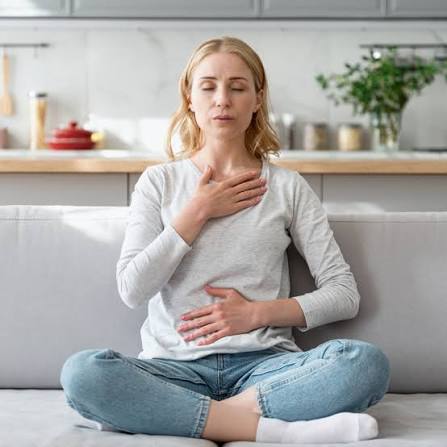 Woman sitting comfortably with hands on chest and abdomen while relaxing into the inhale.