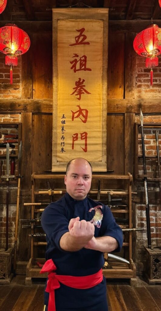 Mark Wiley demonstrating an Ngo Cho Kun posture beneath an Inner Gate Ngo Cho Kun banner.