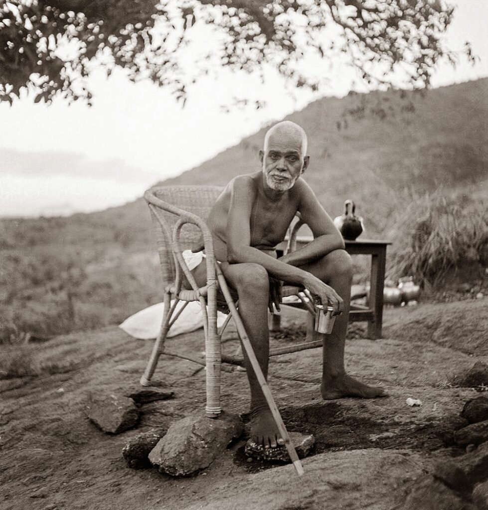 Ramana Maharshi seated outdoors at Arunachala, reflecting his teaching on silence, self-awareness, and turning attention toward the source.